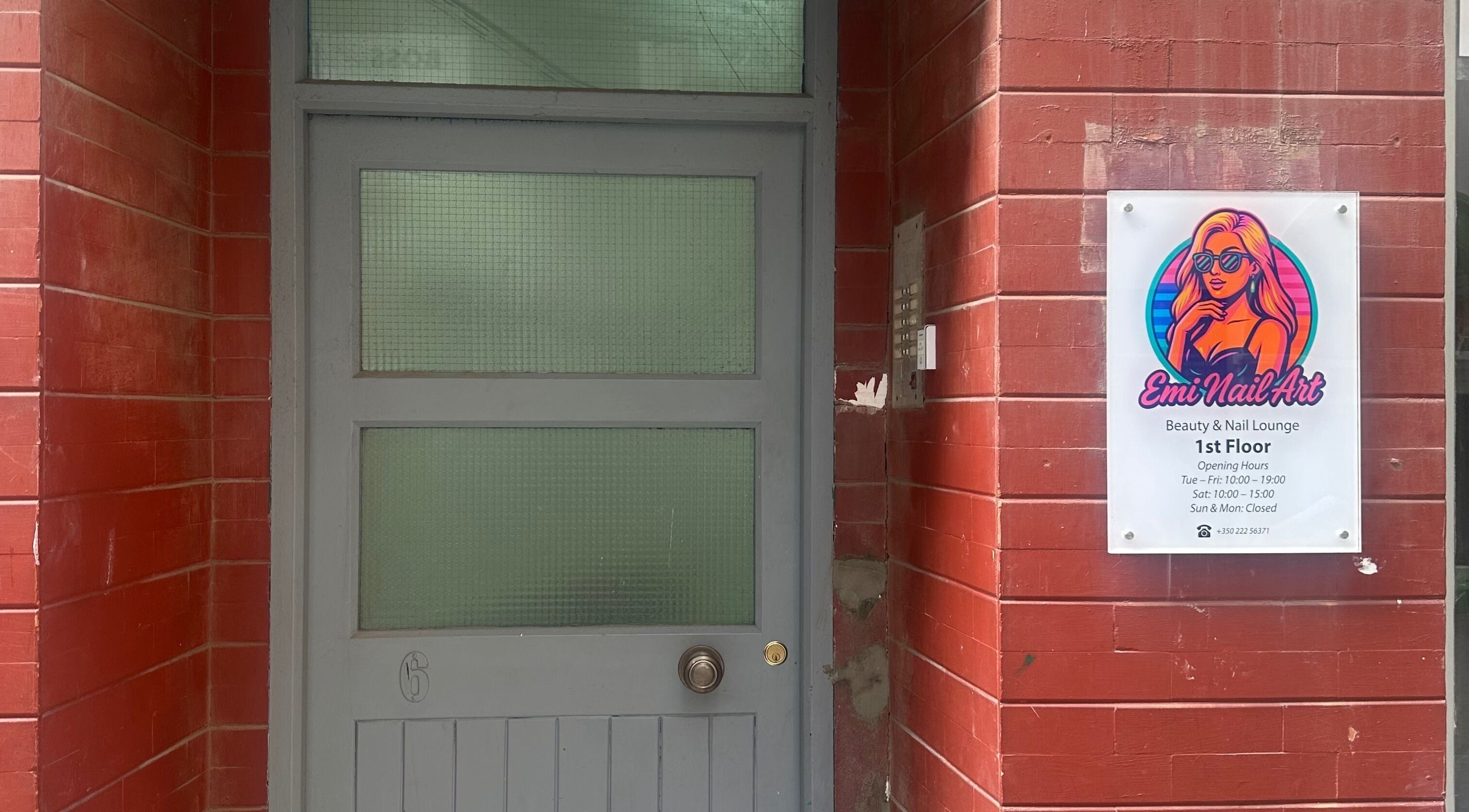 Entrance of Emi Nail Art in Gibraltar, GI with vibrant signage and red brick wall.