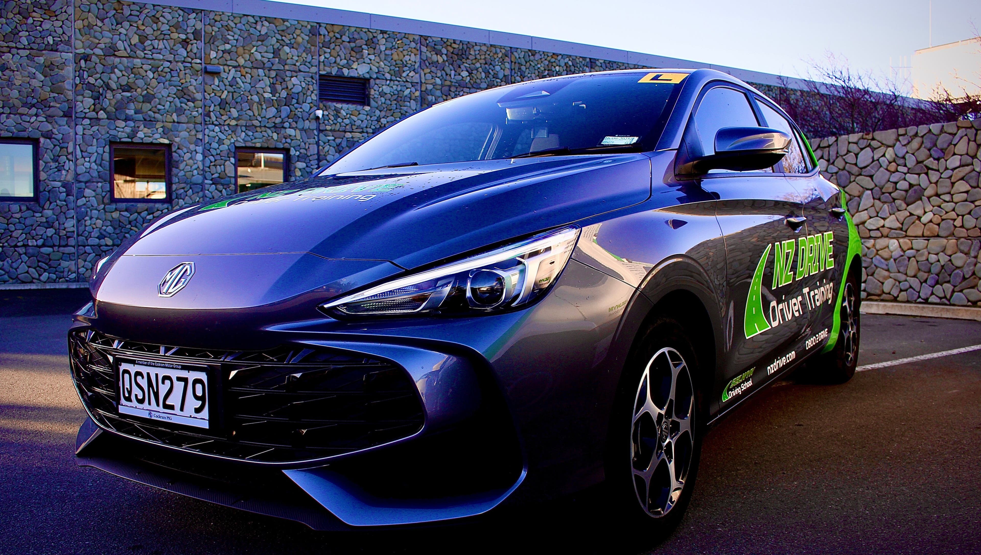 NZ Drive - Selwyn Driving School training car in Rolleston, Canterbury, NZ, parked beside a stone wall.