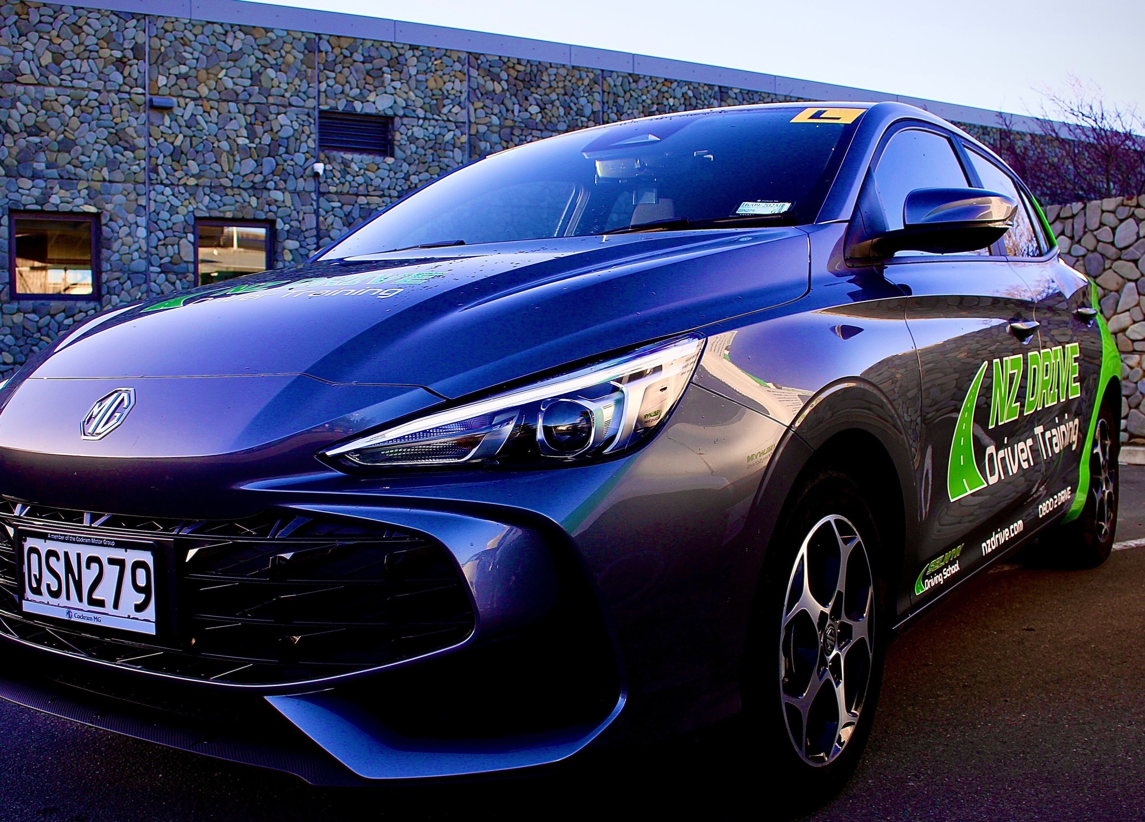 NZ Drive - Selwyn Driving School training car in Rolleston, Canterbury, NZ, parked beside a stone wall.