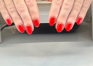 Red manicured nails at Soothe & Glow, Bletchley, England, GB, displayed over a nail dryer.