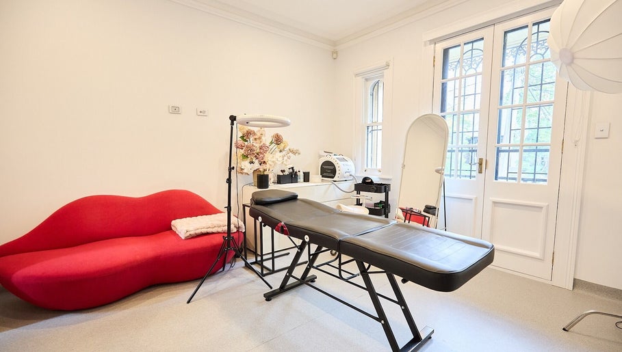 Modern beauty room at Angelina Samko, Bondi Junction, New South Wales, AU with red sofa and massage bed.
