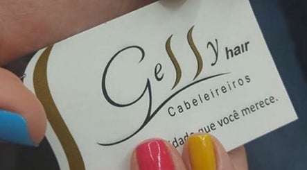 Cartão de visita do Gessy Hair Cabeleireiros em Taubaté, SP, segurado por mãos com unhas coloridas.