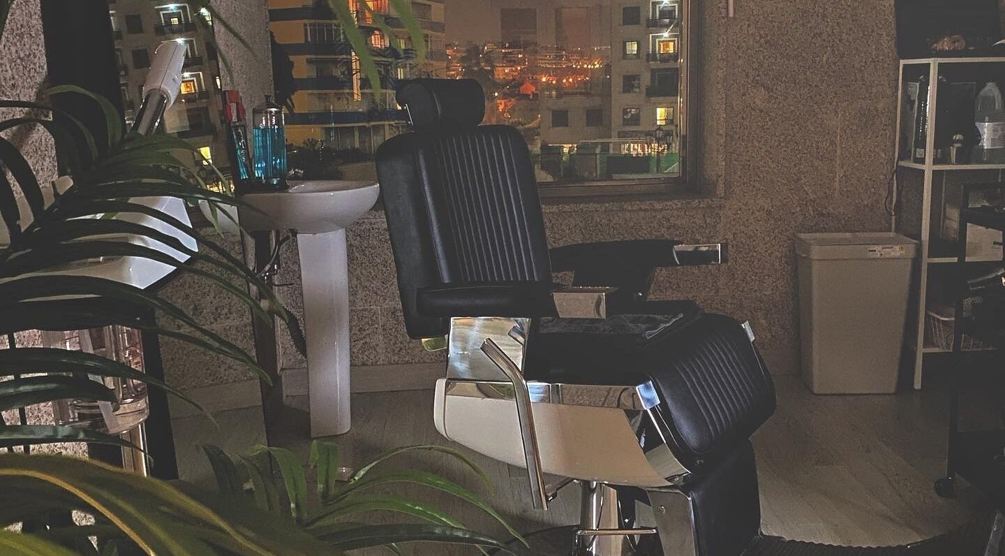 Interior nocturno de Buenos Amigos Barber Studio, Fuengirola, con silla de barbero elegante y vista urbana.