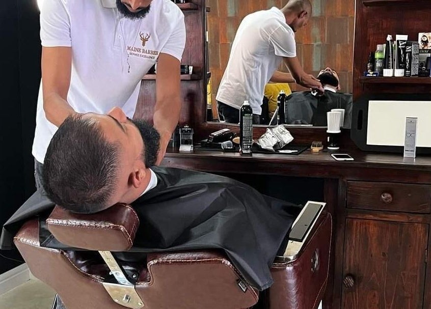 Barber expertly grooms client's beard at Maine Barber, Centurion, Gauteng, ZA. Relaxed atmosphere.