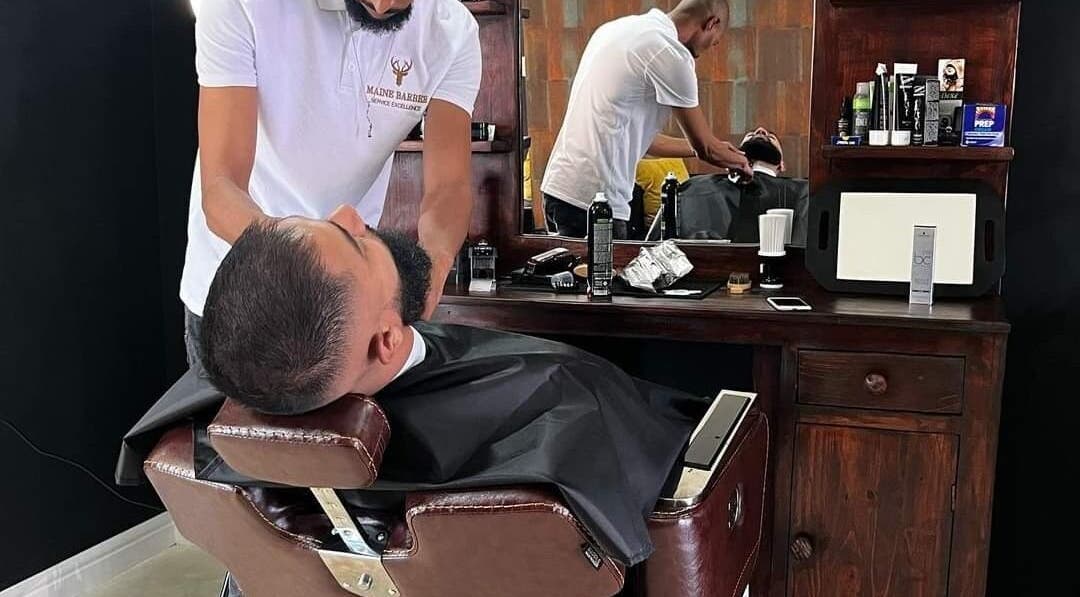 Barber expertly grooms client's beard at Maine Barber, Centurion, Gauteng, ZA. Relaxed atmosphere.