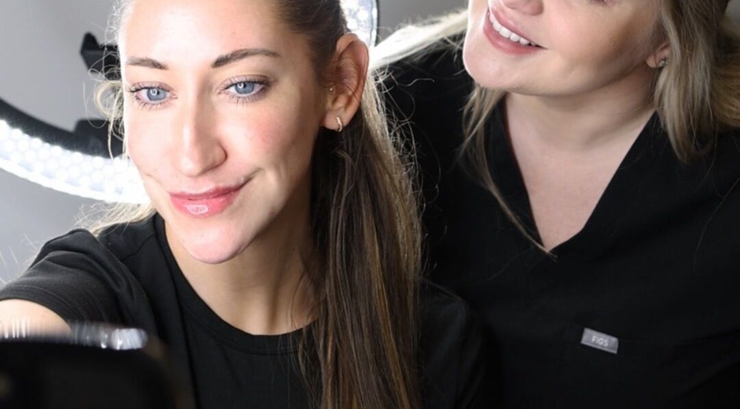 Two women at Impeccable Aesthetics, Warrington, England, GB, smiling during a beauty treatment session.
