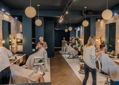 Stylish interior of Hermanos Barbershop Green Point, Cape Town, Western Cape, ZA, with customers getting haircuts.