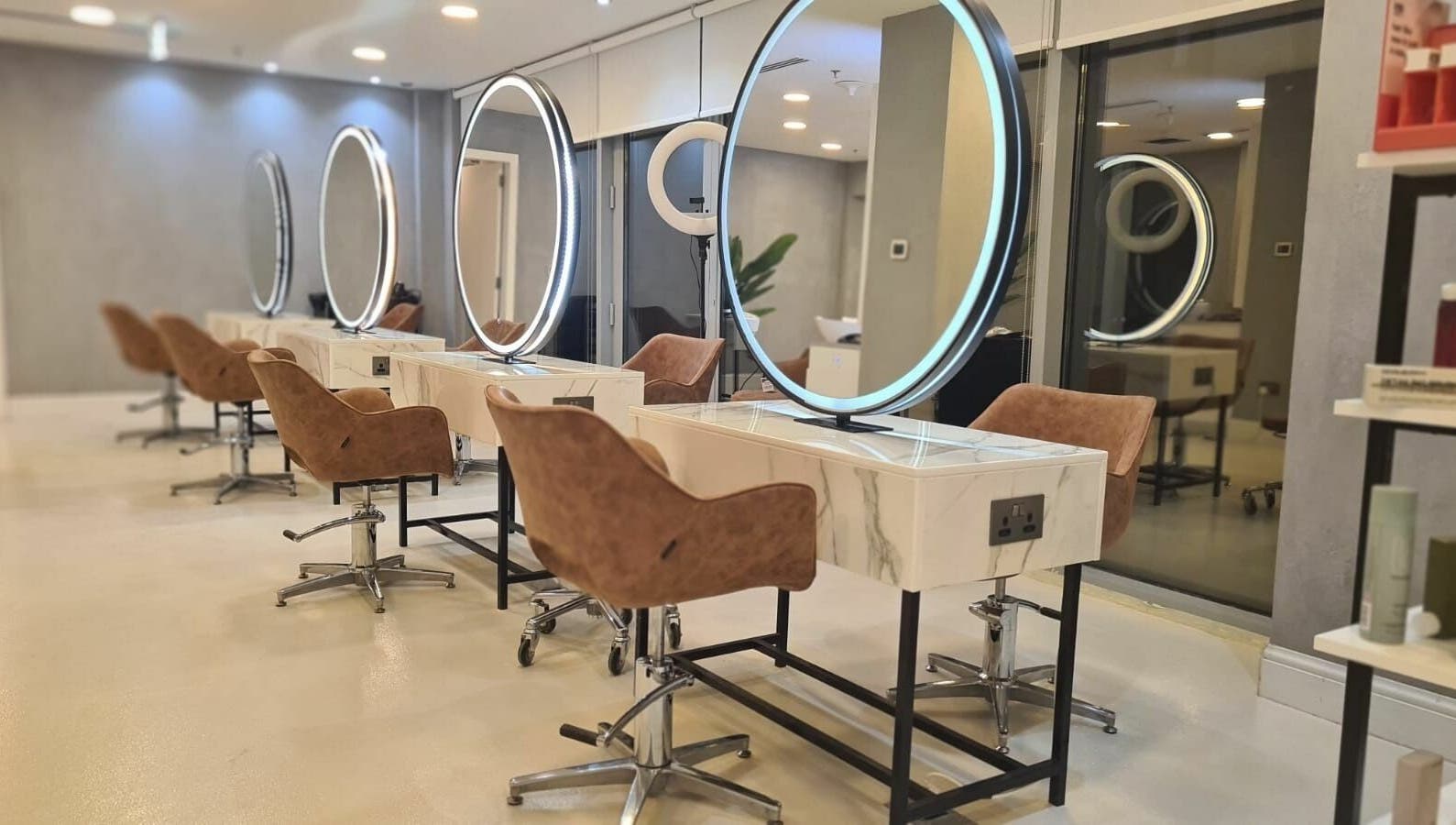 Grafton Salon in Dubai, AE showcases its chic mirrored workstations and plush brown chairs for a luxurious experience.
