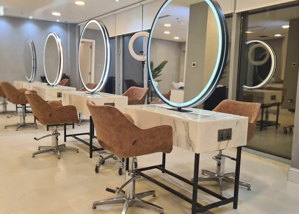 Grafton Salon in Dubai, AE showcases its chic mirrored workstations and plush brown chairs for a luxurious experience.
