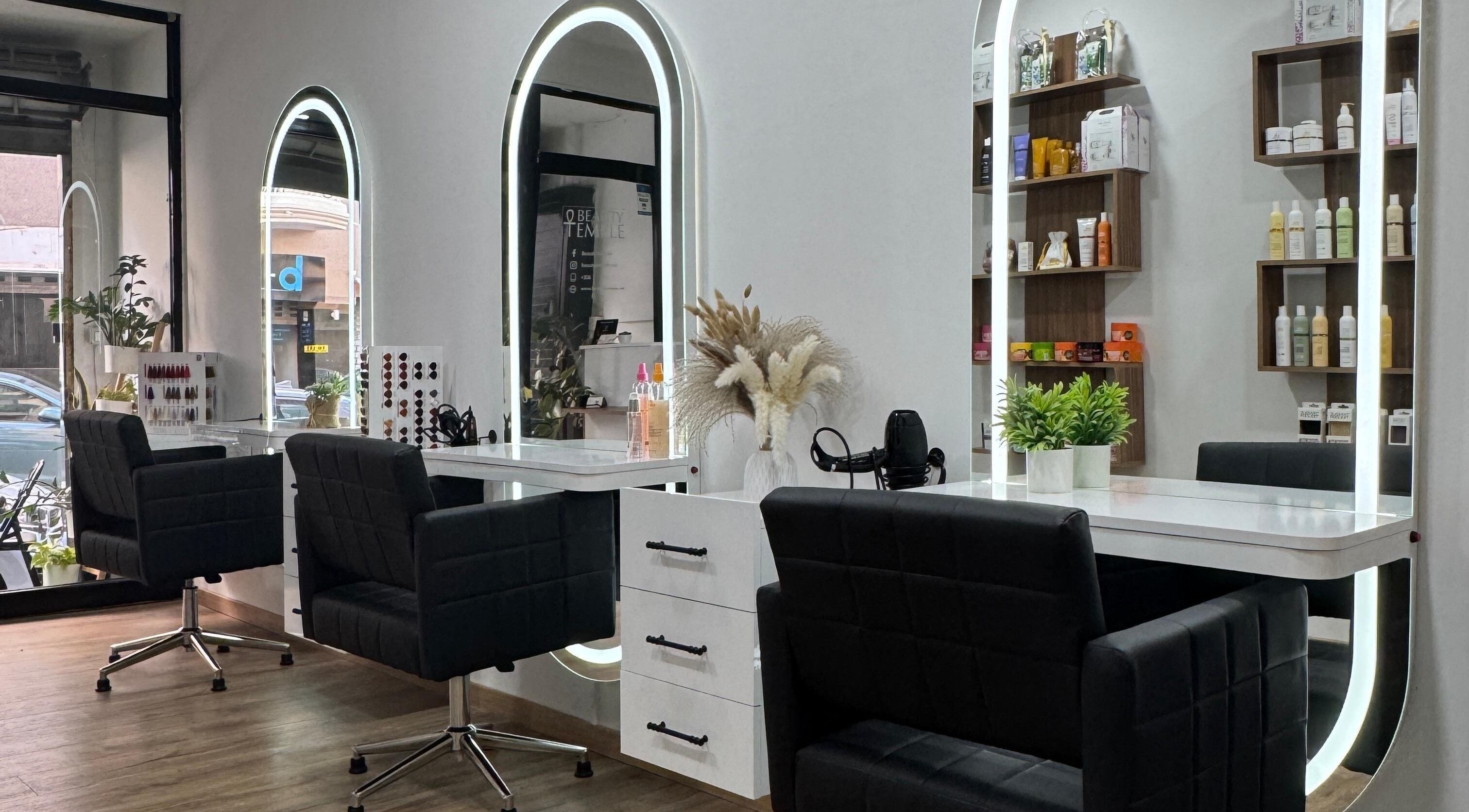 Elegant salon setup at Beauty Temple, San Ġwann, MT with chic black chairs and illuminated mirrors.