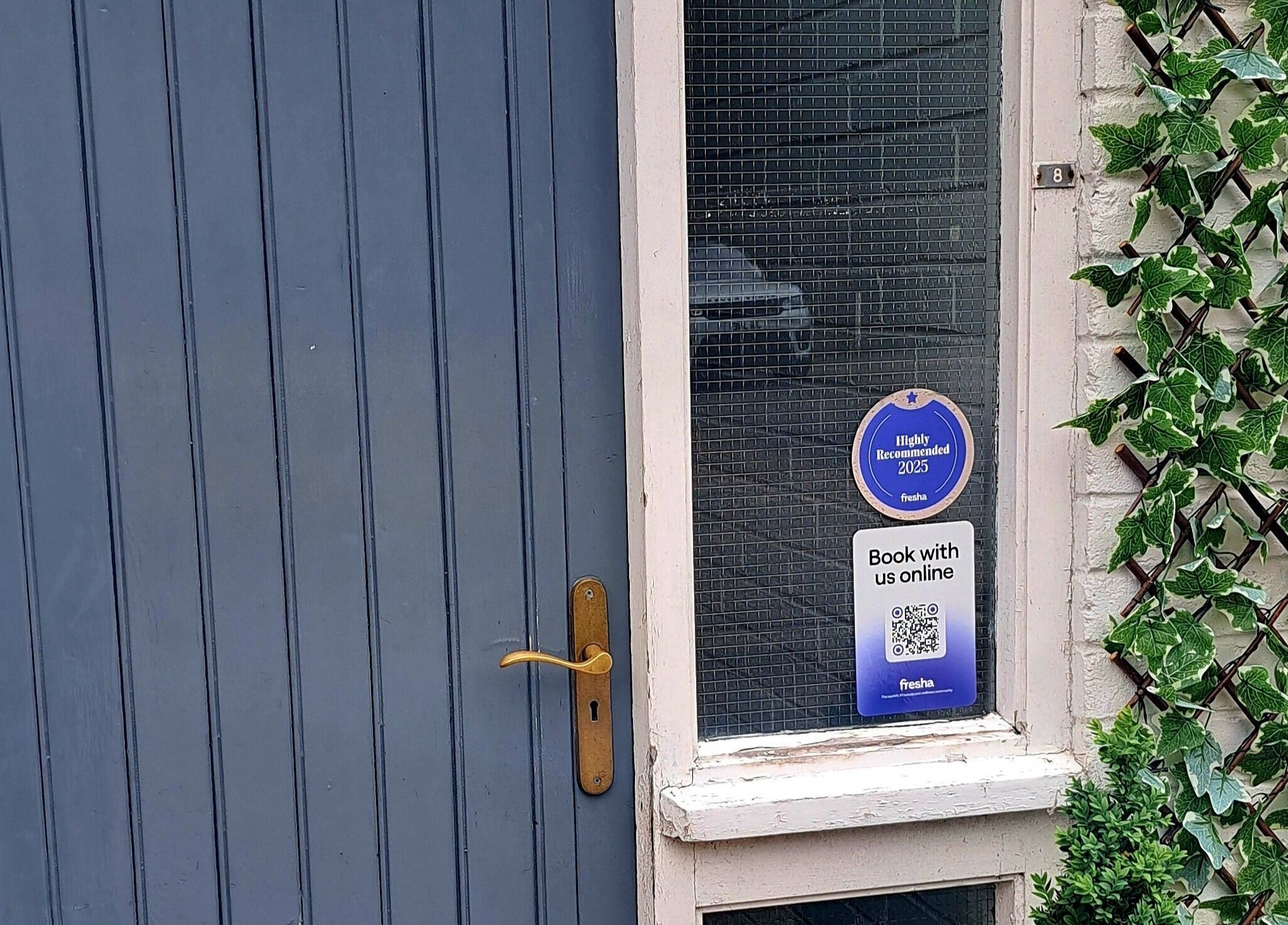 Entry door of Bespoke Beauty SP, Newton-Le-Willows, England, GB with lush greenery and booking sign.
