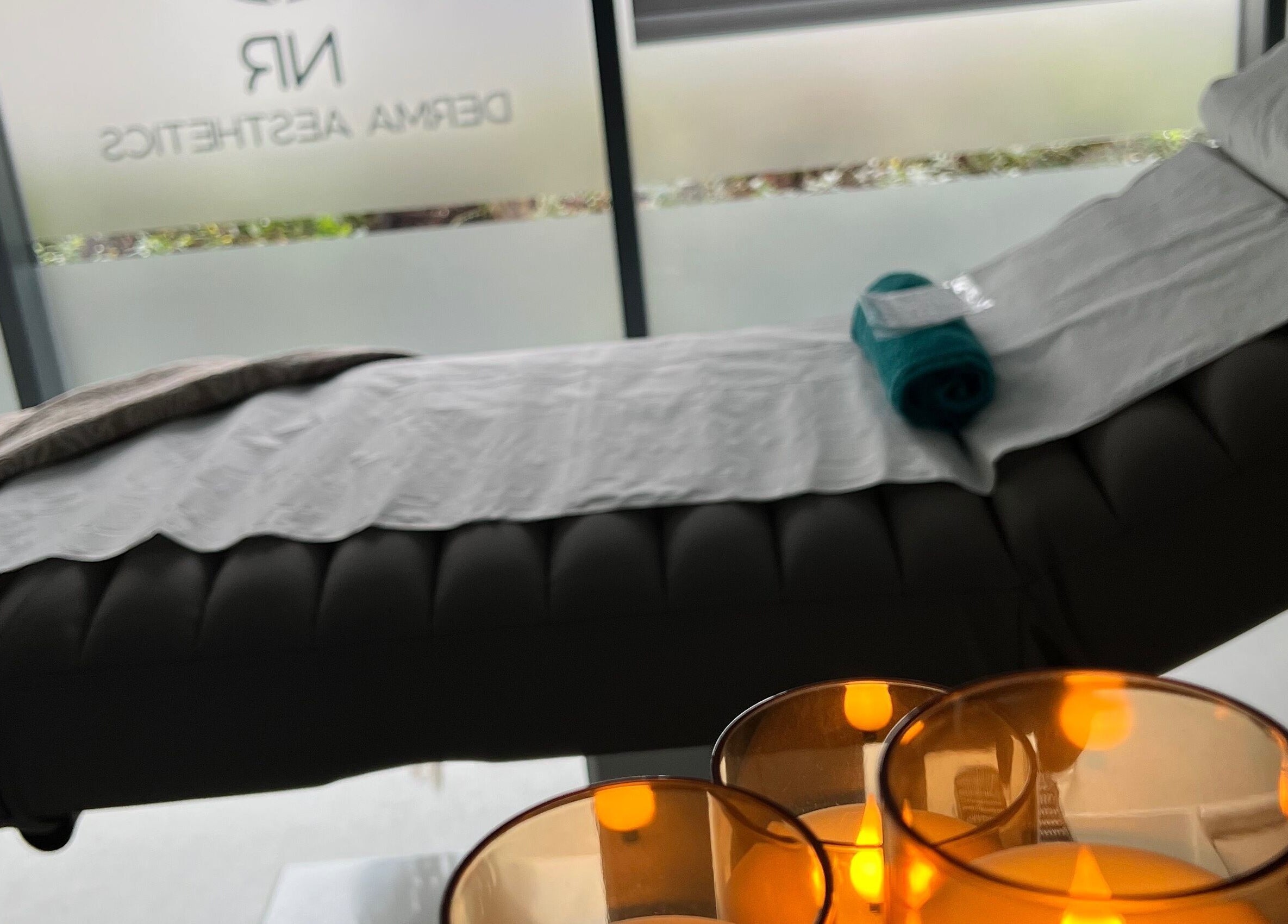 Relaxing treatment room at NR Derma Aesthetics in Bicester, England, GB with a cozy massage table and ambient candles.