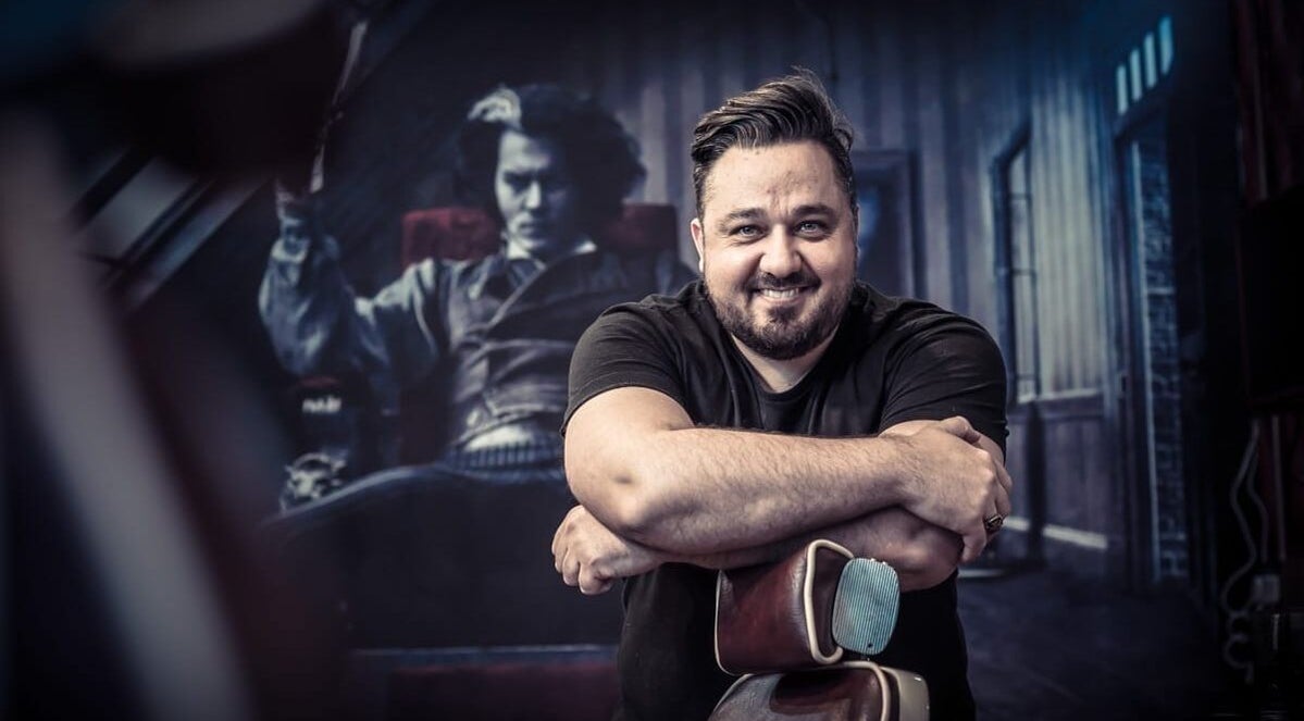 A smiling barber in Brazuca B1 Barbers, Carlisle, England, GB, showcasing unique style.