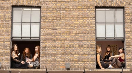Women sitting in windows at Tattoo Like a Girl Club, Dublin, County Dublin, IE against a brick wall backdrop.