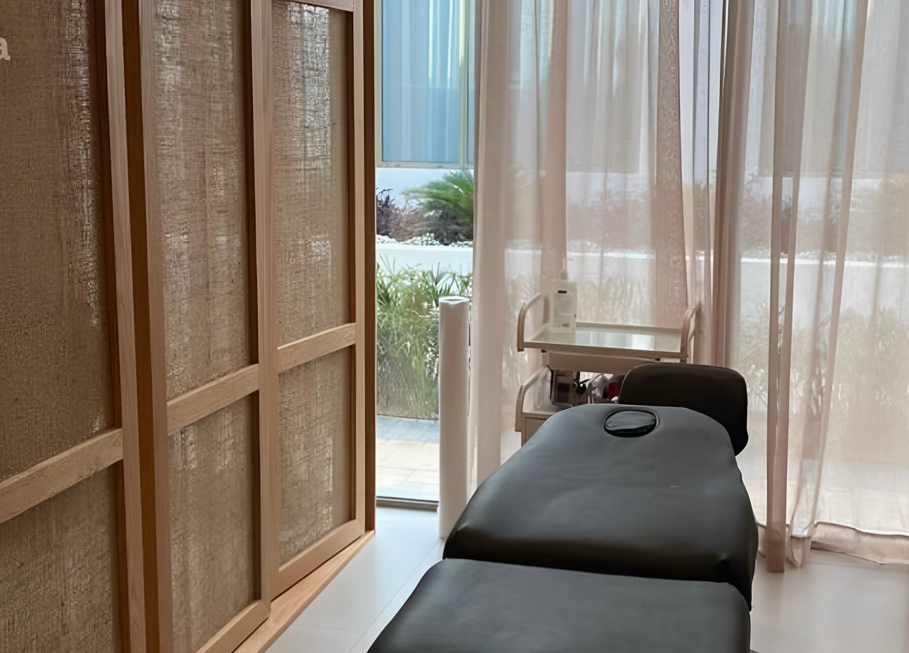 Relaxing massage room at Zoz Lashes - Dariyah, Diriyah, SA with soft light through curtains and cozy treatment bed.