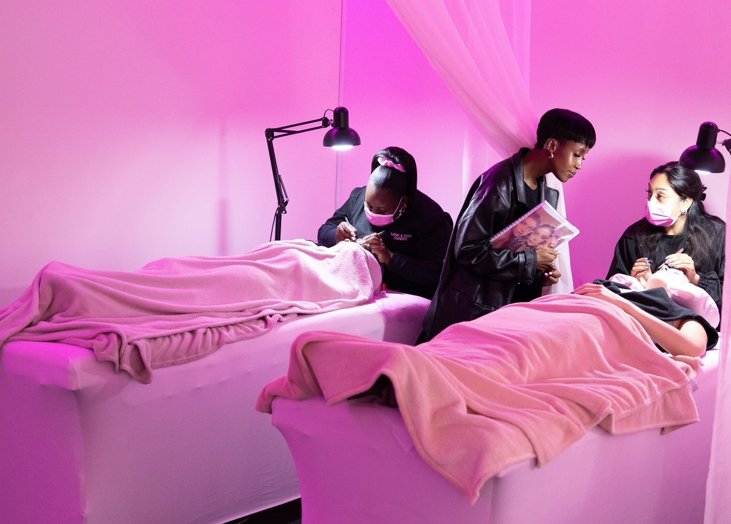 Professionals applying eyelash extensions at Lash and Dash, Sandton, Gauteng, ZA in a tranquil, pink-lit room.