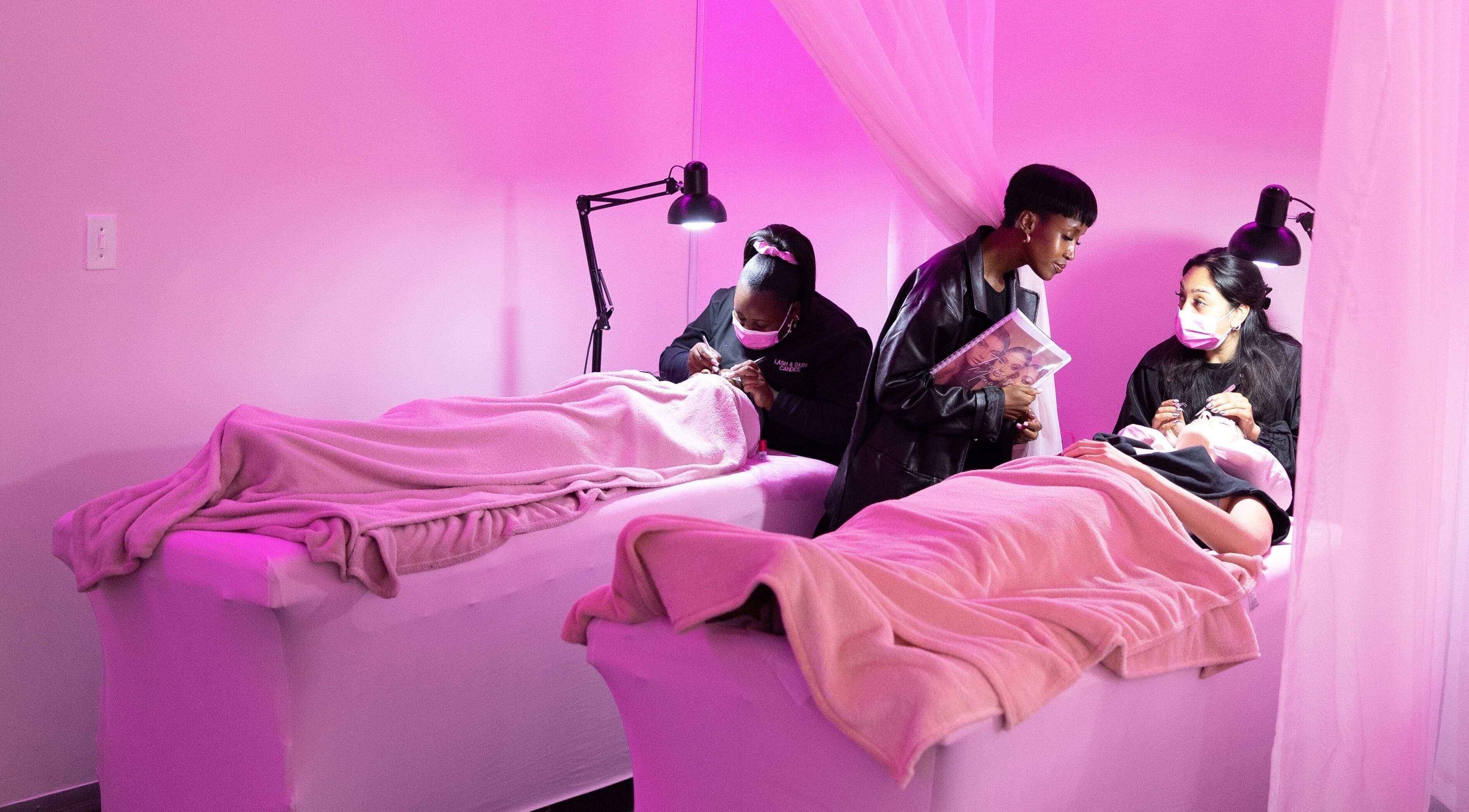 Professionals applying eyelash extensions at Lash and Dash, Sandton, Gauteng, ZA in a tranquil, pink-lit room.