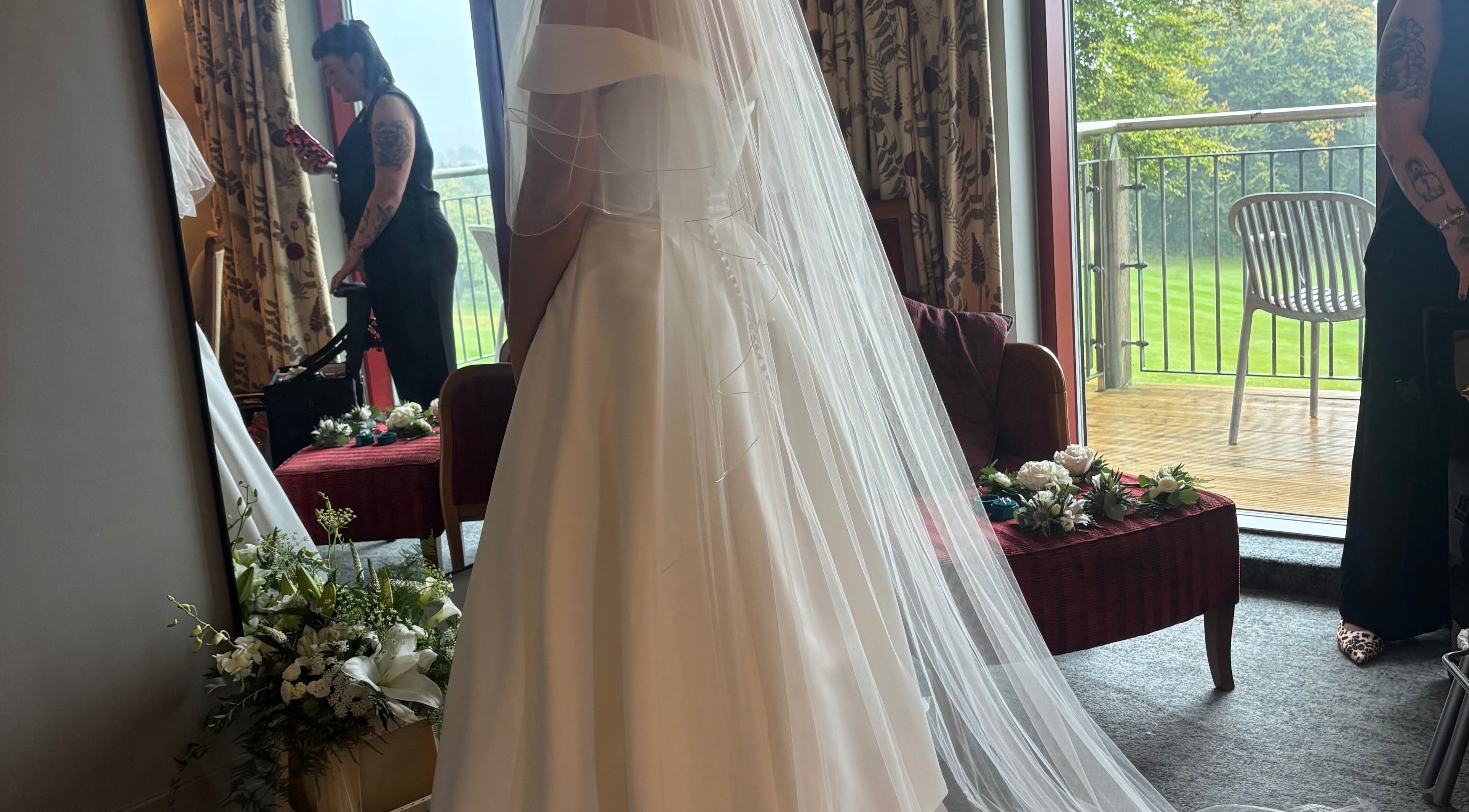 A bride in a flowing gown stands at Beautilocks in Trelewis, Wales, GB, near a window with scenic views.