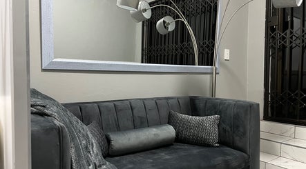 Cozy lounge area at Ash Ed Beauty Suite in Germiston, Gauteng, ZA, with a plush gray sofa and modern lighting.