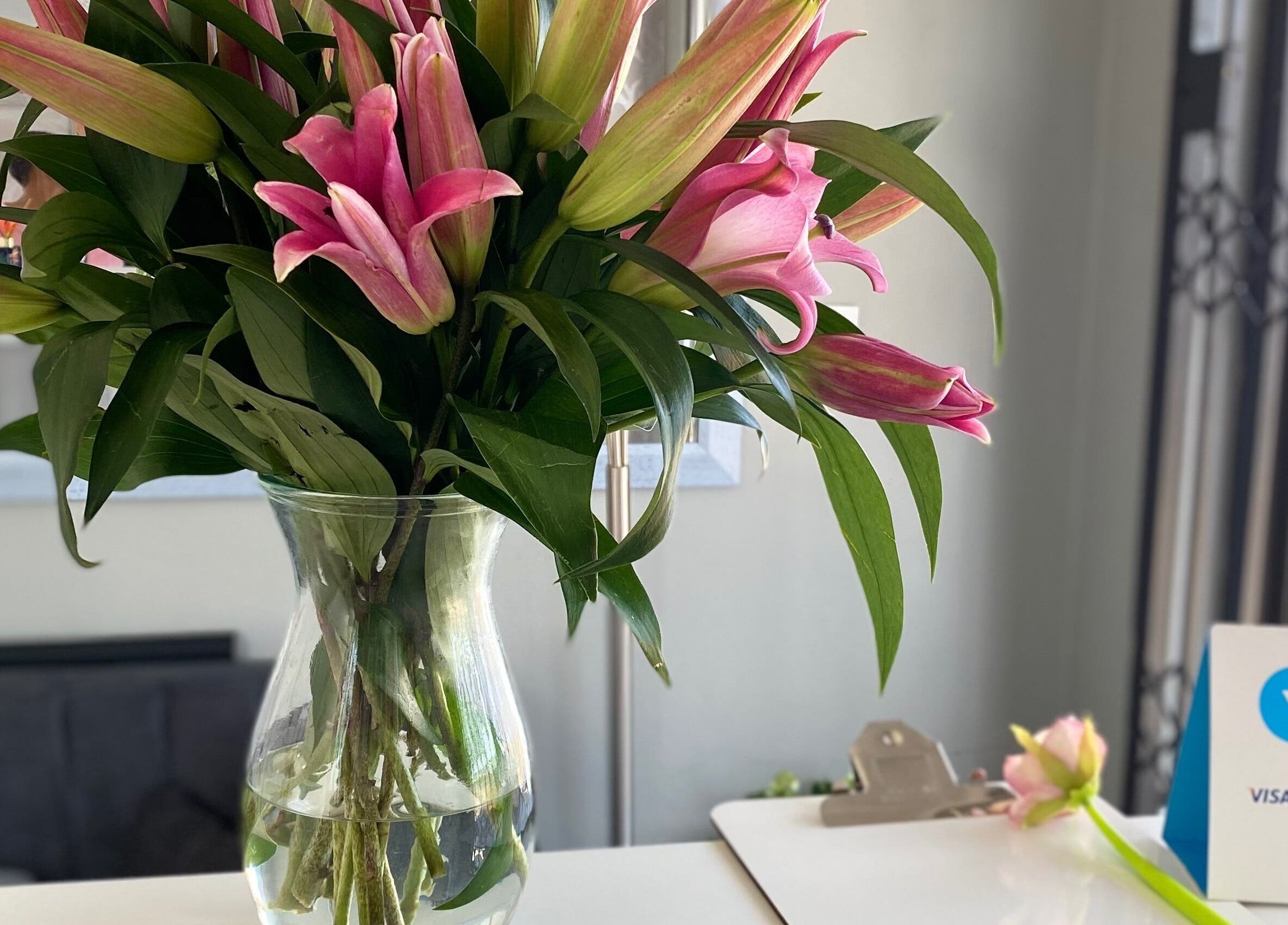 Vibrant pink lilies in a glass vase at Ash Ed Beauty Suite, Germiston, Gauteng, ZA, creating a welcoming atmosphere.