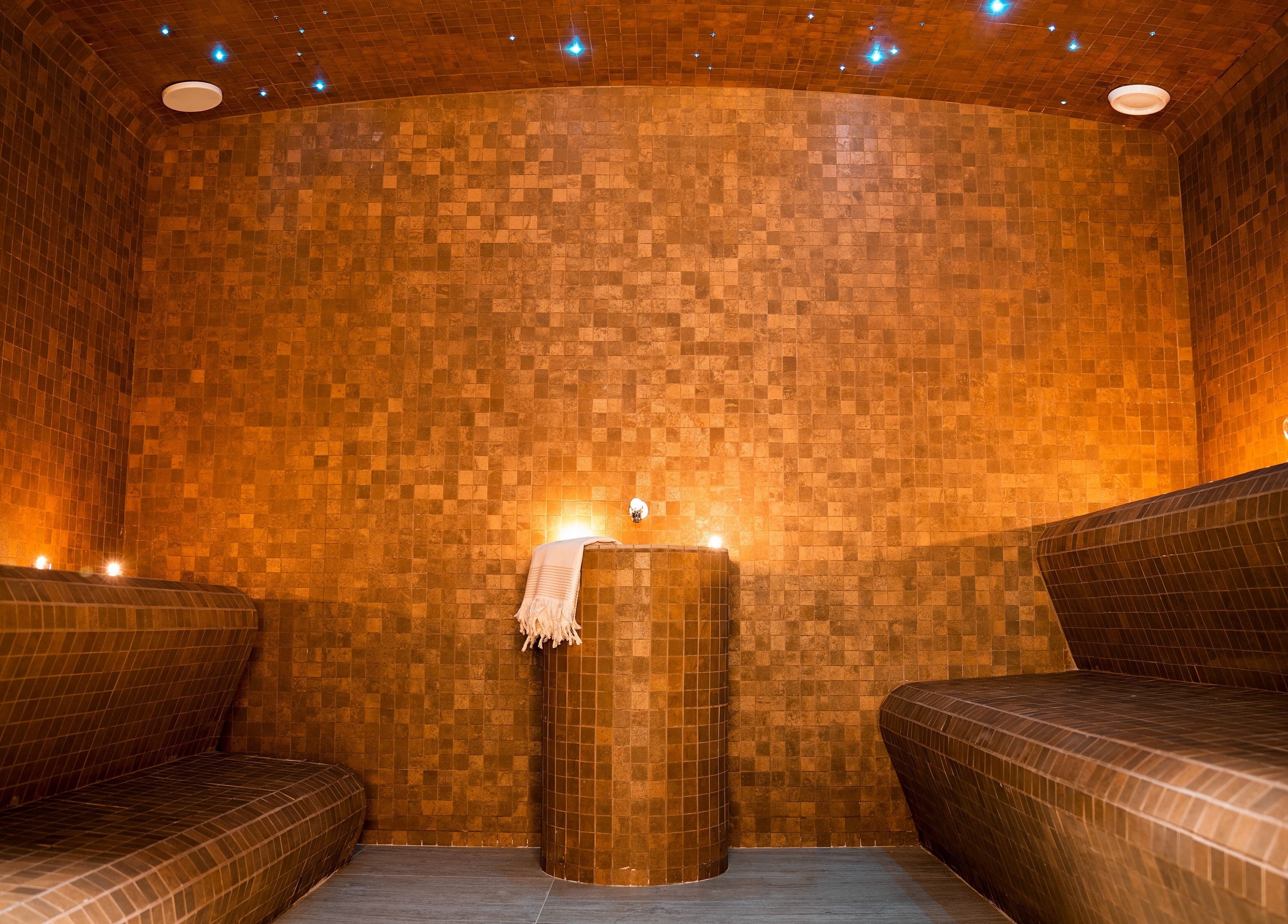 Relaxing hammam room at E1 Spa and Wellness, Gibraltar, GI with warm amber lighting and smooth tiled seating.