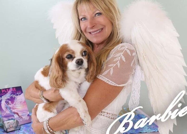Woman in angel wings holding dog at AngelHairBarbie-SanibelFit4Life, Sanibel, Florida, US.