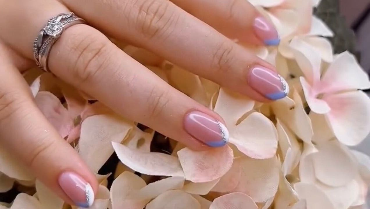 Stylish nail art at Cove Beauty Co, Poole, England, GB, showcasing blue-tipped French manicure on floral background.