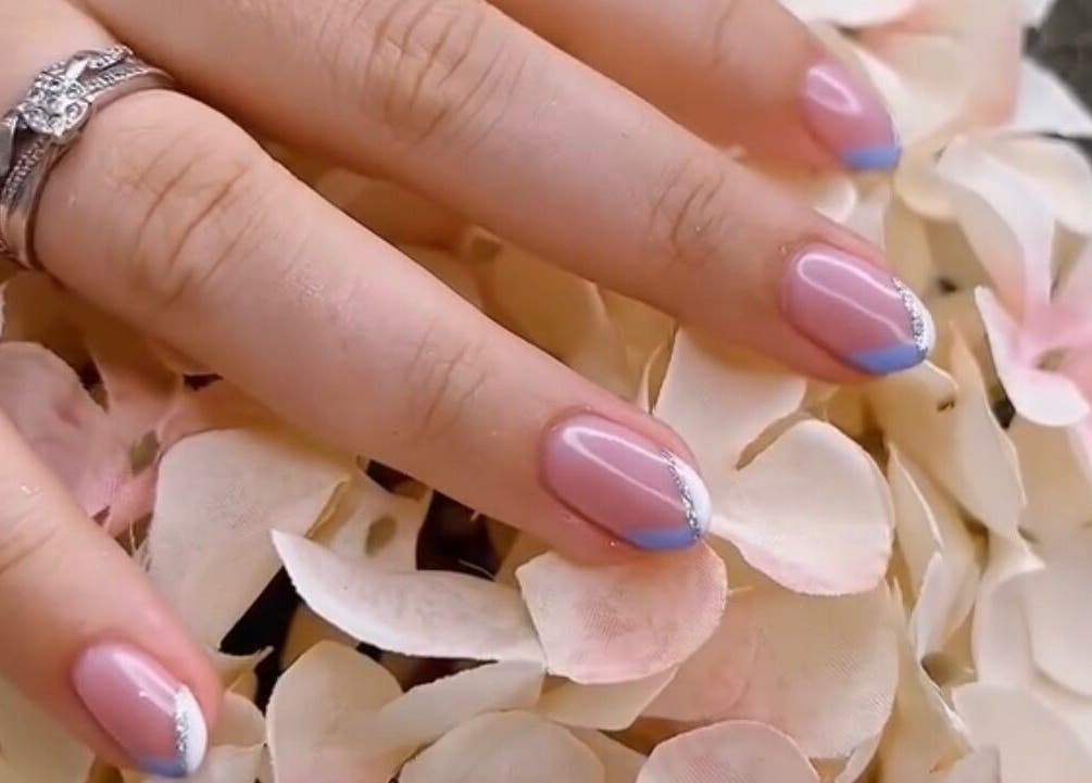 Stylish nail art at Cove Beauty Co, Poole, England, GB, showcasing blue-tipped French manicure on floral background.