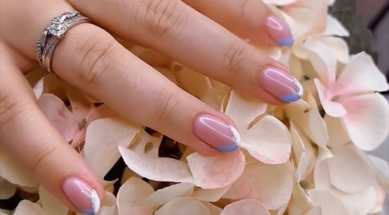 Stylish nail art at Cove Beauty Co, Poole, England, GB, showcasing blue-tipped French manicure on floral background.