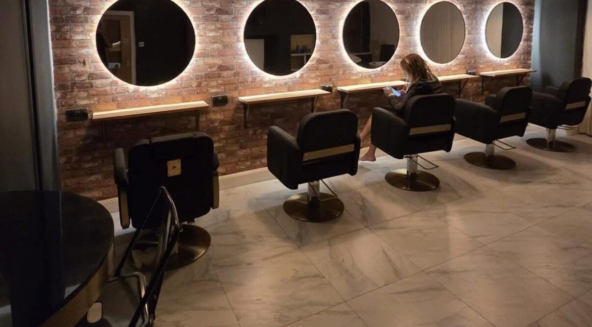 The Elite Studio in Thetford, England, GB: stylish salon with modern chairs and circular mirrors on brick wall.