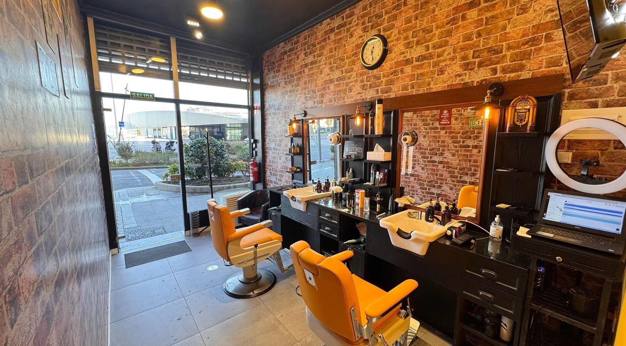 Interior acogedor de Barberia Oro Negro (via norte) en Vigo, ES, con sillas naranjas y paredes de ladrillo.