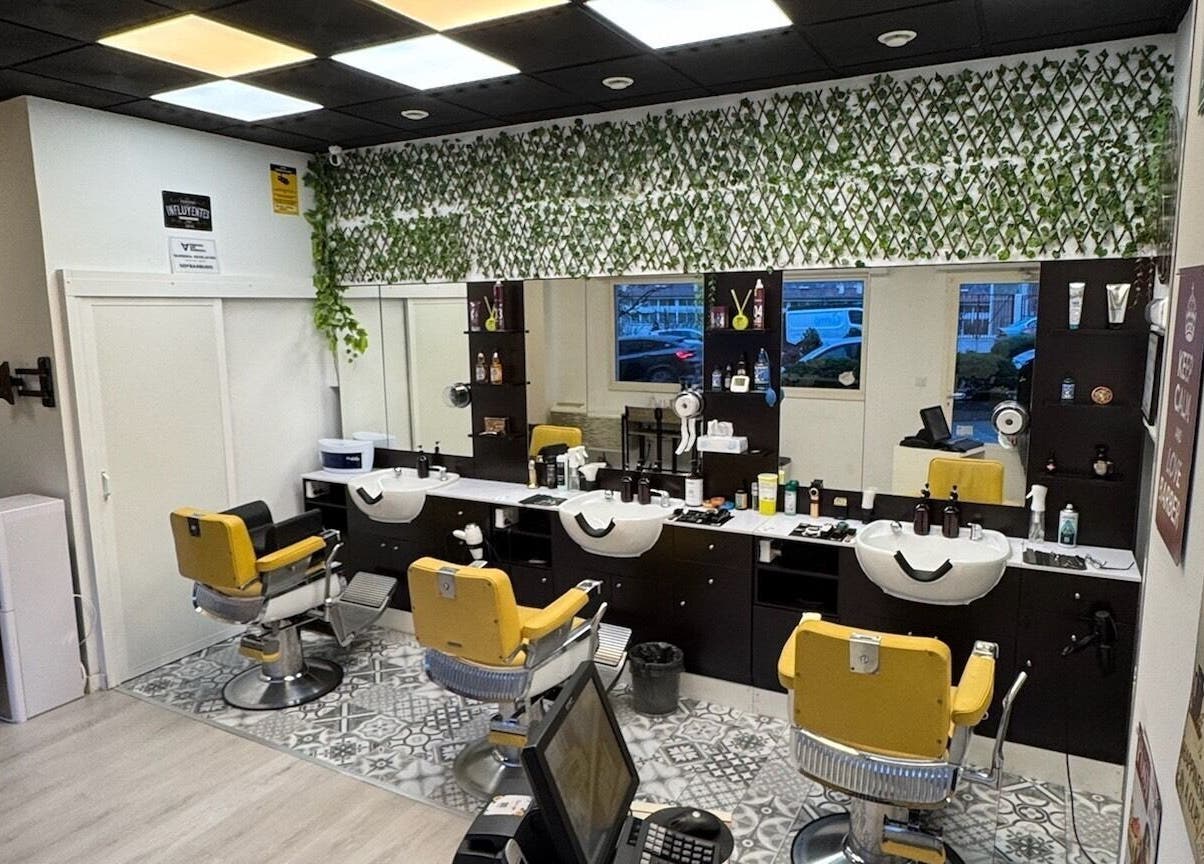 Interior de Barberia Oro Negro en Vigo, ES, con sillas amarillas y decoración verde en el salón.