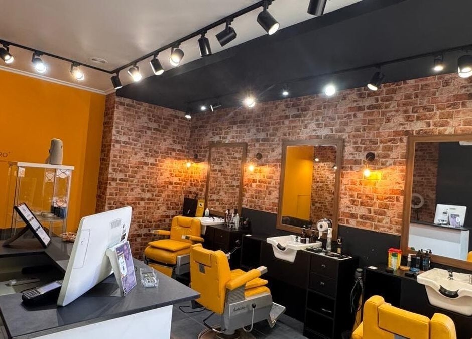 Interior moderno de Barberia Oro Negro en Vigo, ES, con sillas amarillas y paredes de ladrillo.