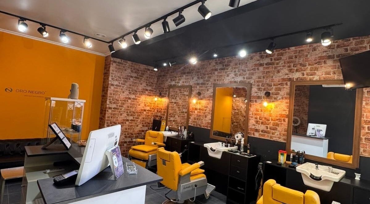 Interior moderno de Barberia Oro Negro en Vigo, ES, con sillas amarillas y paredes de ladrillo.