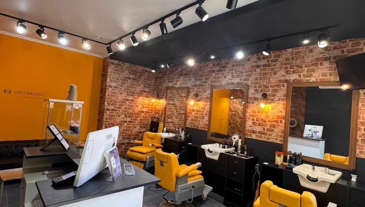 Interior moderno de Barberia Oro Negro (Salamanca) en Vigo, ES, con sillas amarillas y paredes de ladrillo.