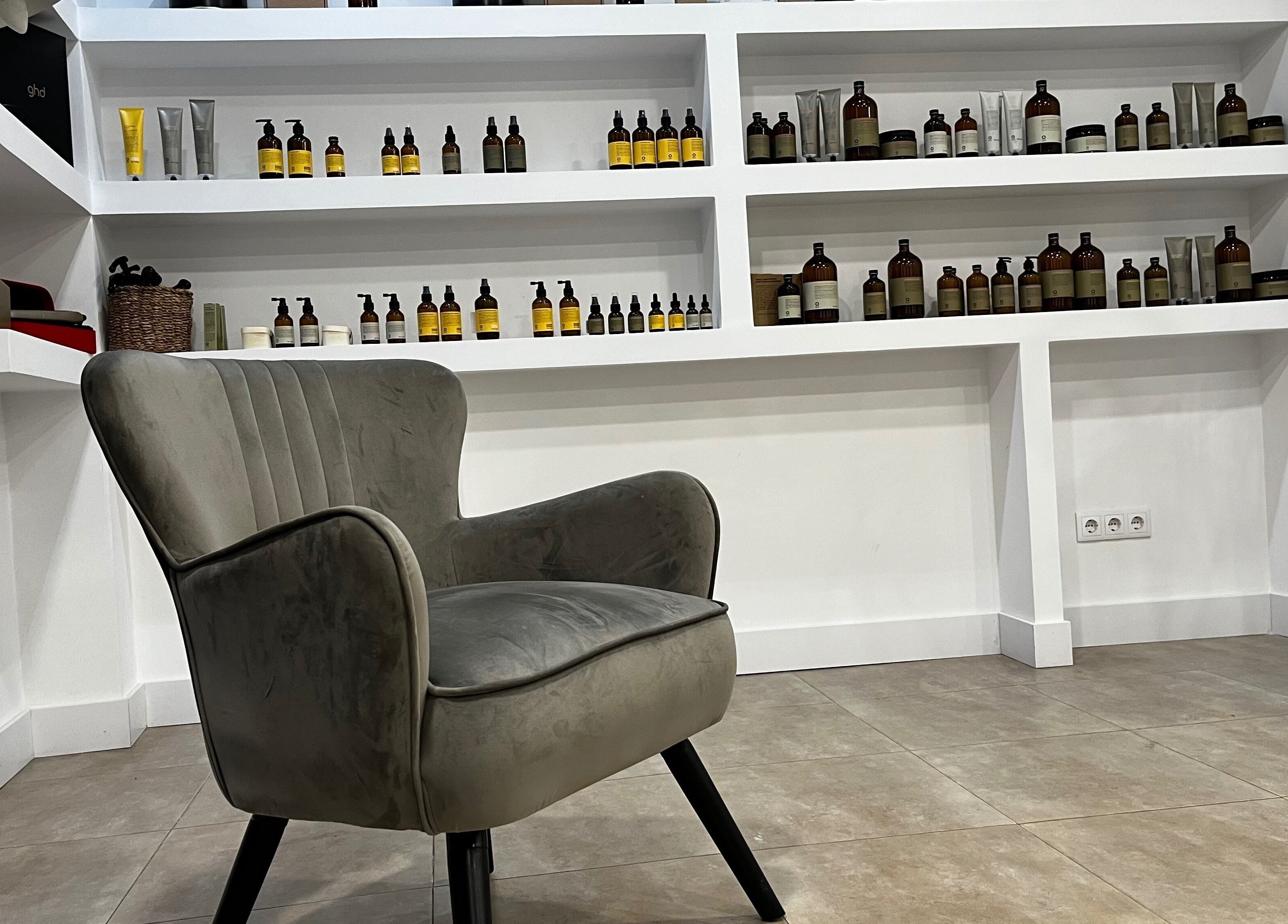 Silla moderna en R Estilistas, Alacant, Comunidad Valenciana, ES, con estanterías de productos de belleza.