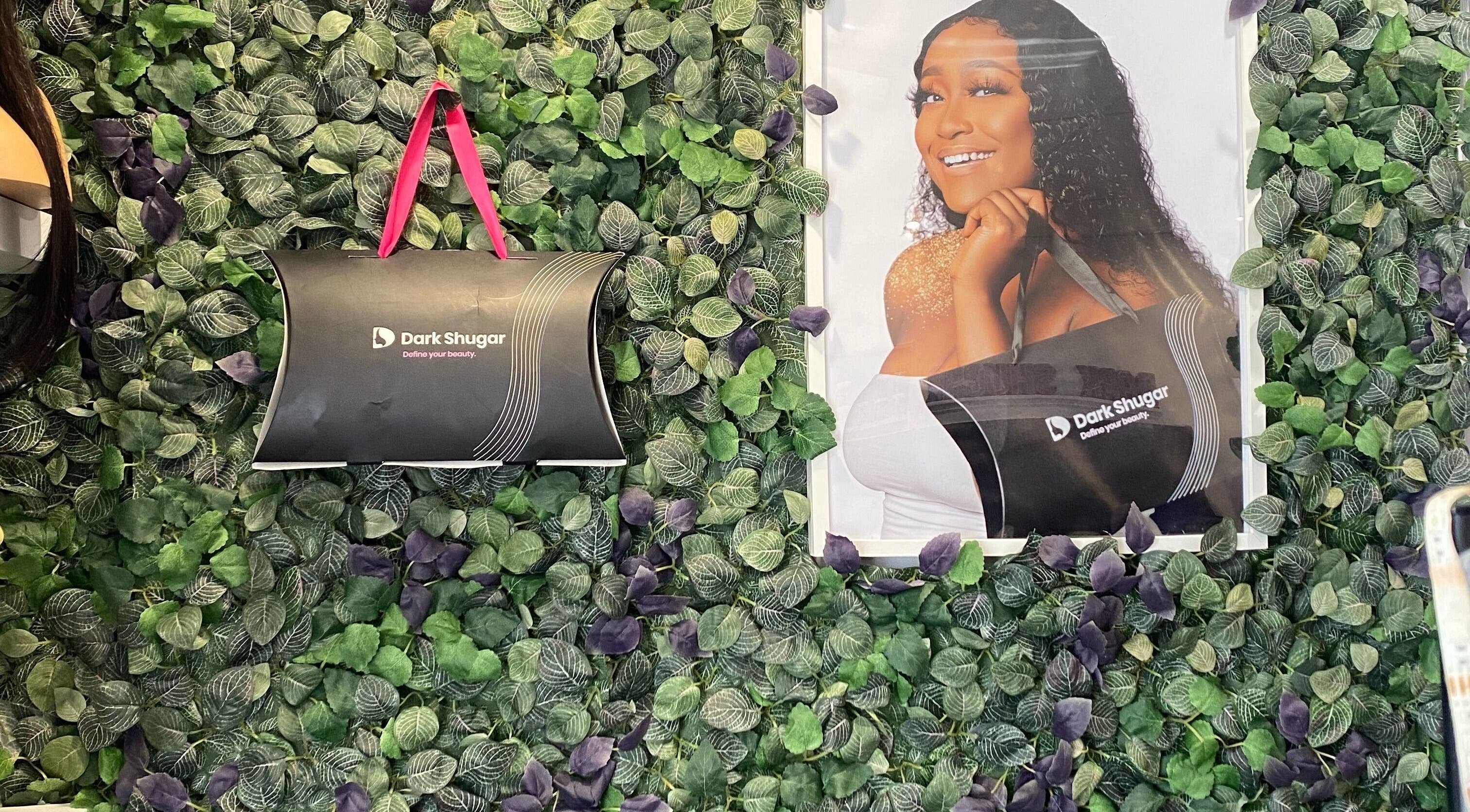 Green leaf-covered wall with Dark Shugar branding at Dark Shugar Hair & Beauty Studios, Ellice, Winnipeg, Manitoba, CA.