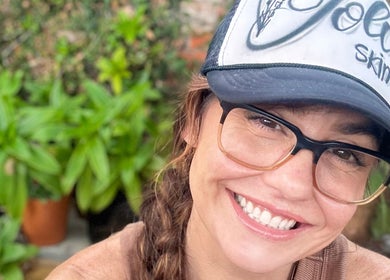 Smiling person in a Jolie Skin Studio cap at Jolie Skin Studio, Austin, Texas, US surrounded by green plants.