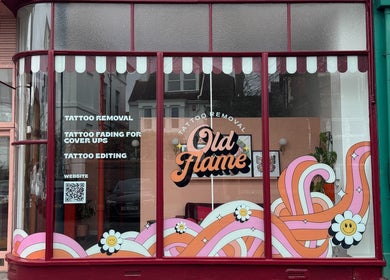 Vibrant storefront of Old Flame Tattoo Removal in Portsmouth, England, GB with colorful signs and designs.