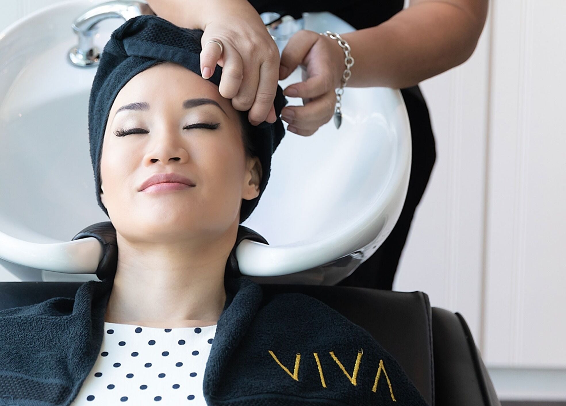 A client enjoys a hair wash at Viva salon in Singapore, SG. Draped in a black towel with Viva logo.