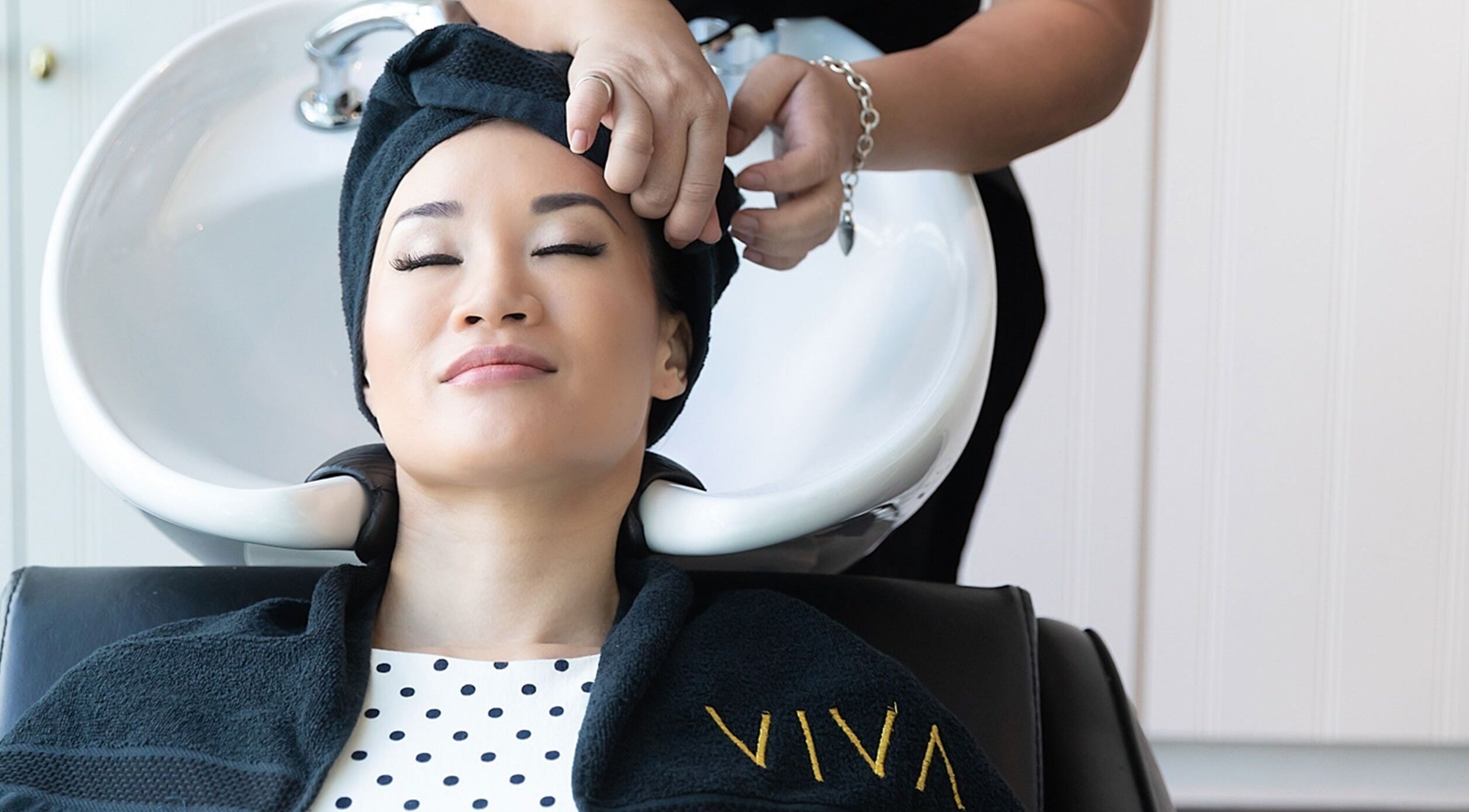 A client enjoys a hair wash at Viva salon in Singapore, SG. Draped in a black towel with Viva logo.