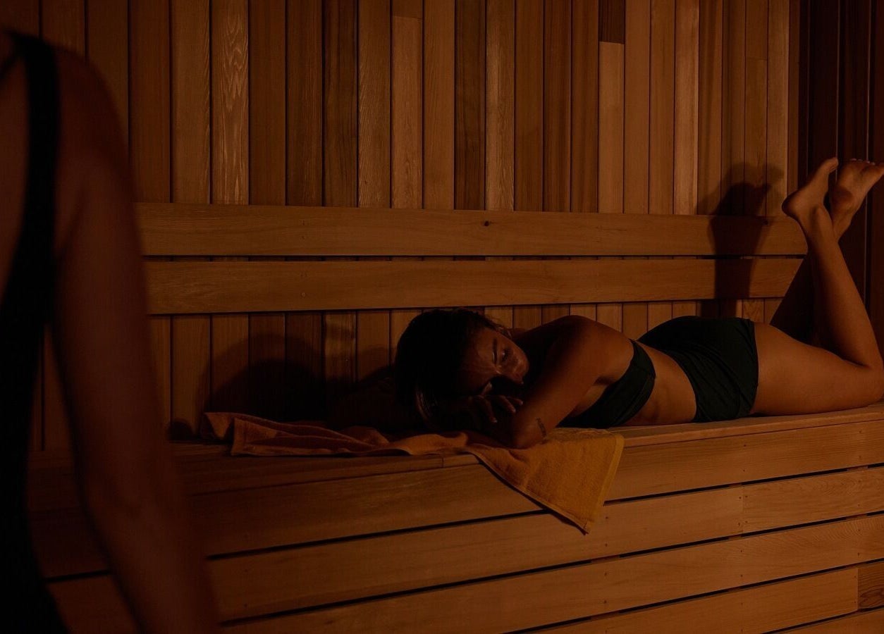Woman relaxing in a sauna at Comma Byron Bay, located in Byron Bay, New South Wales, AU, on a wooden bench.