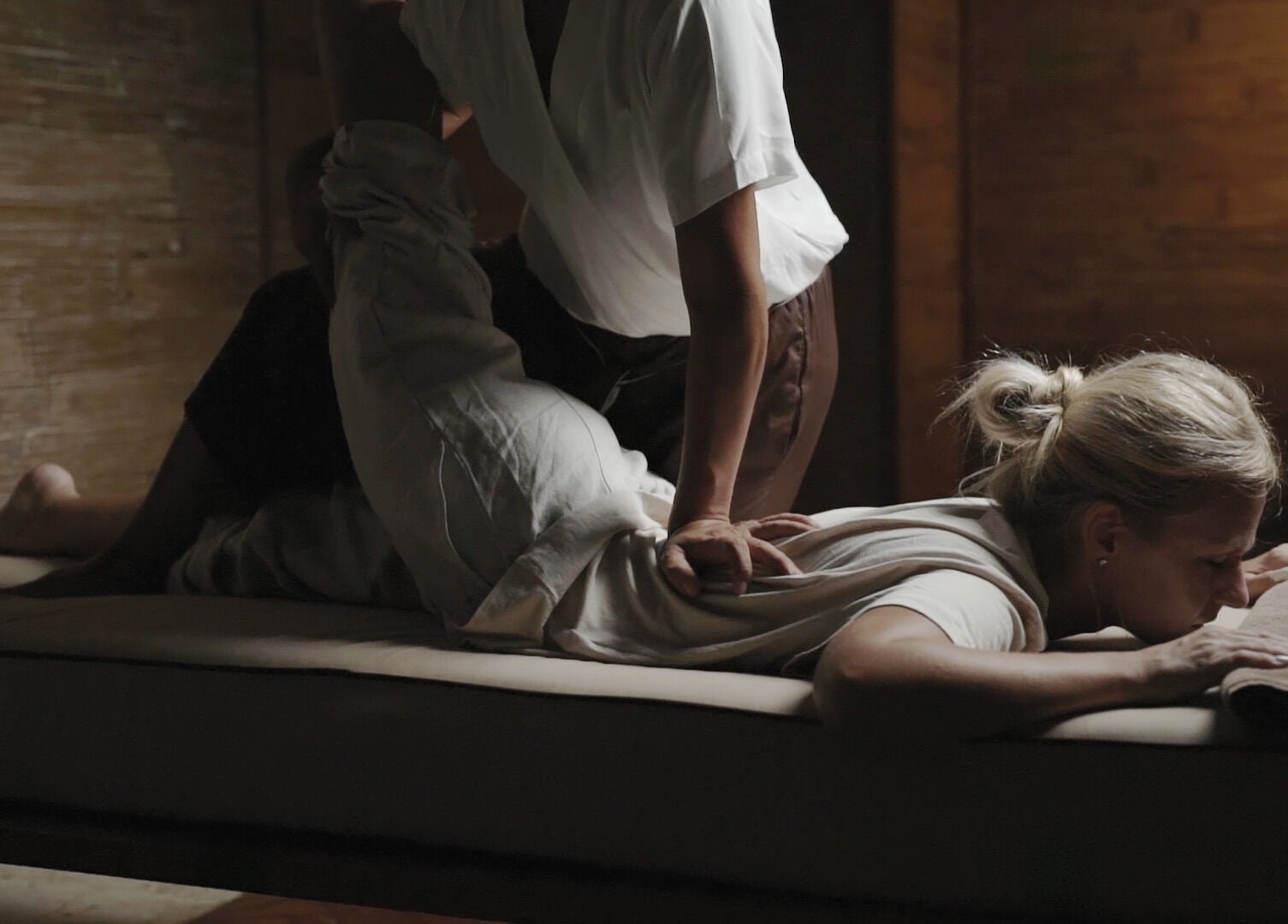 A soothing massage session at Koya Spa, Bali, Bali, ID. Therapist stretching a client on a wooden treatment bed.