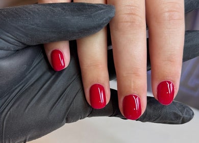 Manicure with red nails at Annabelle’s Beauty, Camberley, England, GB. Nails held by gloved hands.