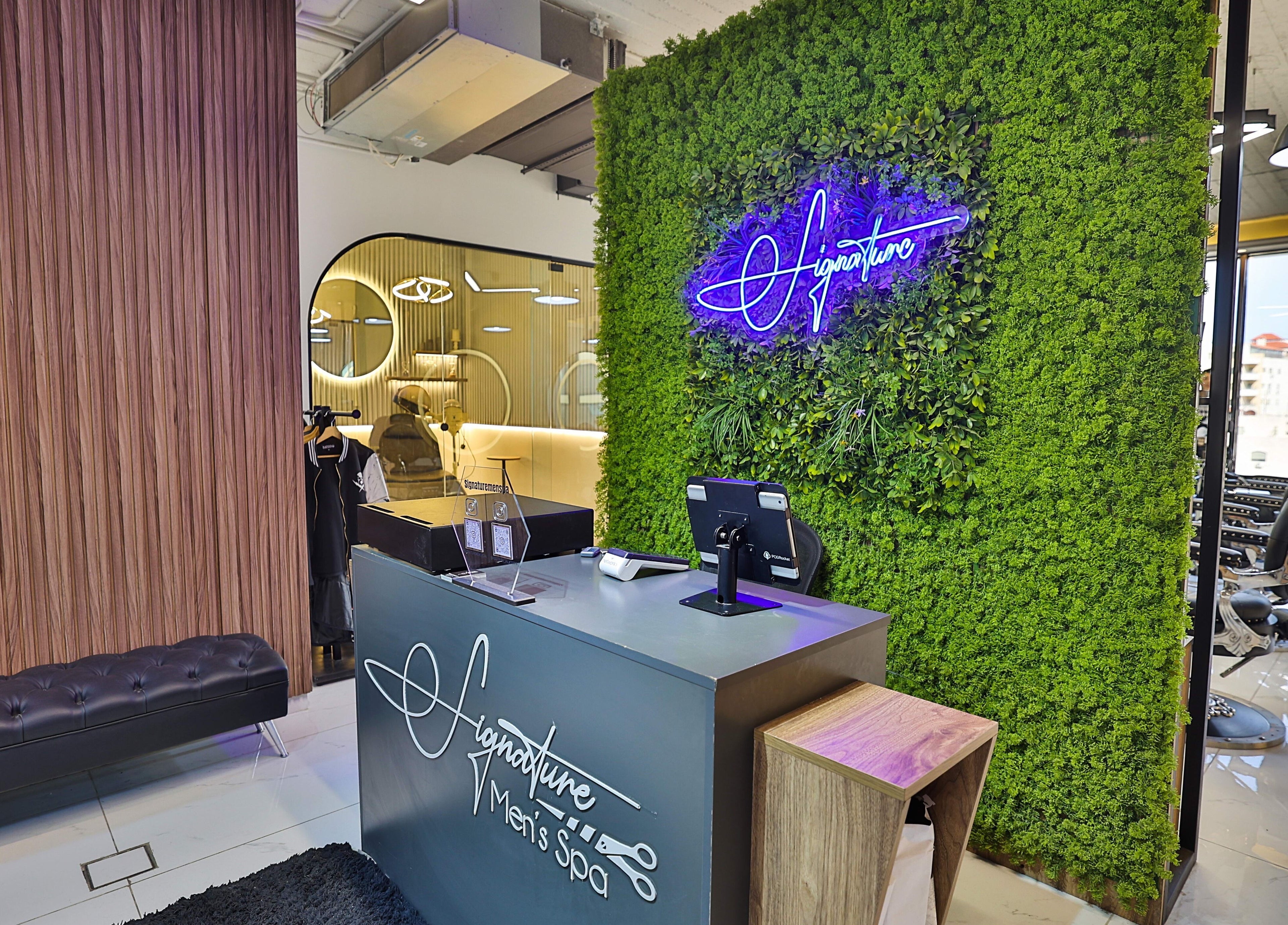 Reception area of Signature Men's Spa By Mostafa in Amman, featuring a lush green wall and sleek design.