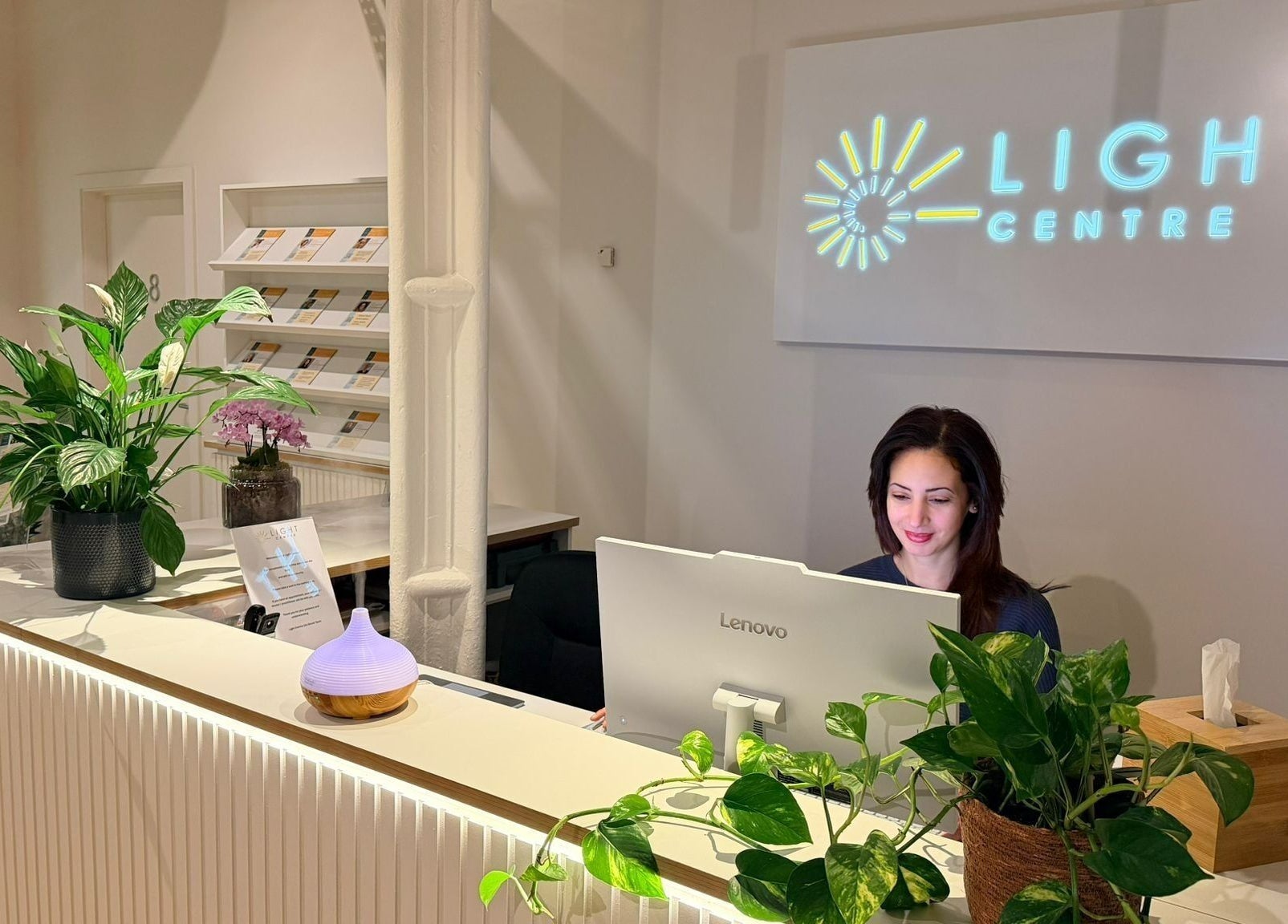 Reception desk at Maen (Men) Old Street, London, England, GB with a woman working and lush green plants.
