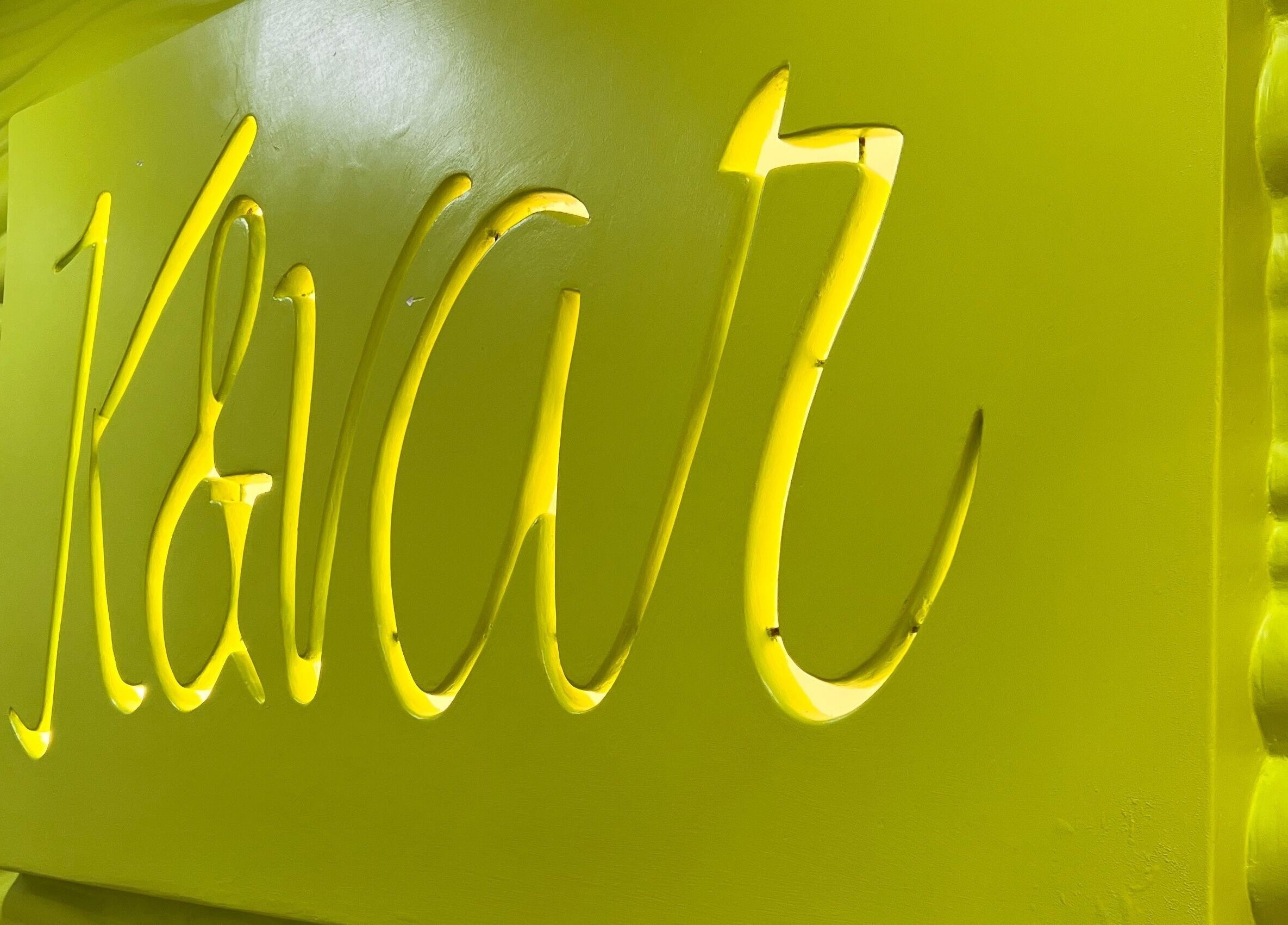 Logotipo amarillo de K&Var Spa Trigal en Valencia, Carabobo, VE con fondo ondulado.