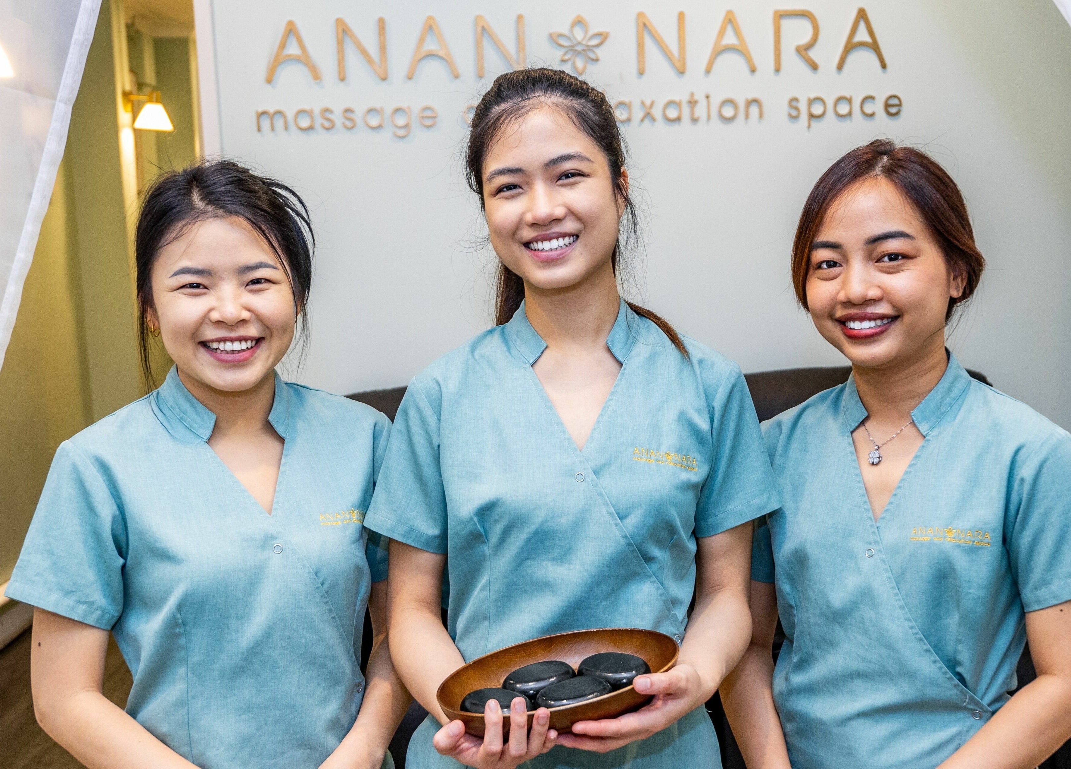 Smiling team at Anan Nara Massage and Relaxation Space in Glebe, New South Wales, AU, with massage stones.