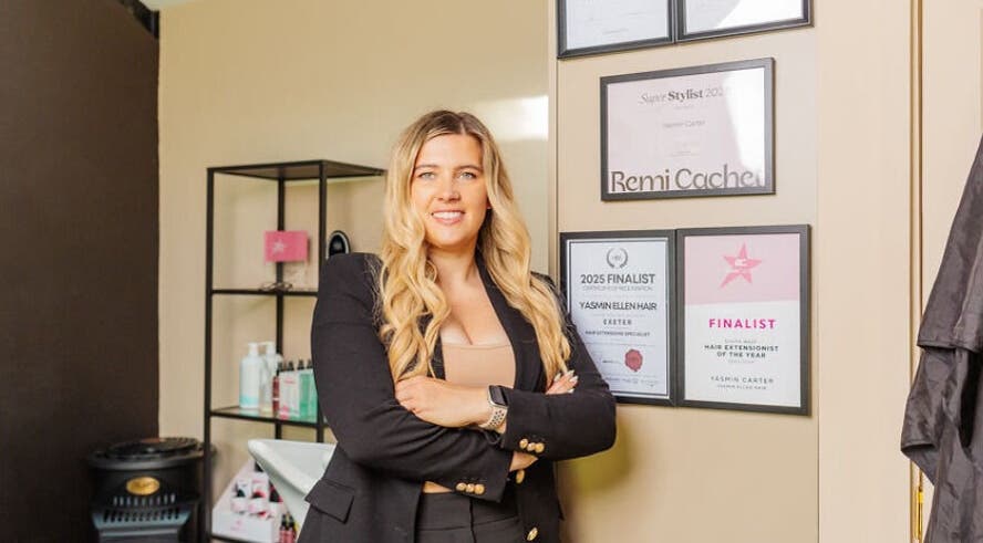 Stylist at Yasmin Ellen Hair in Cullompton, England displaying certificates of excellence on salon wall.
