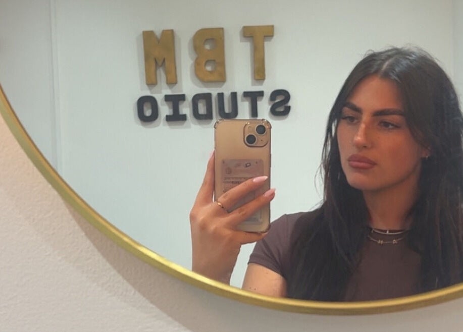 Woman taking mirror selfie at TBM Studio in Bolton, England, GB, with TBM Studio sign in the background.